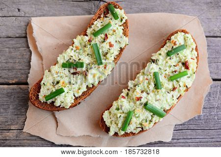 Rye bread toast with sauce guacamole, fresh green onion and dried herbs on a paper. Vegan toast idea for a picnic, breakfast or lunch. Easy avocado recipe. Top view