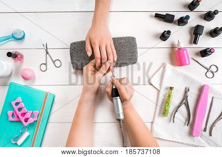 Manicure for the client. Close-up of the hands of a manicurist and client on a wooden background. Nail care. Manicure set and nail polish.