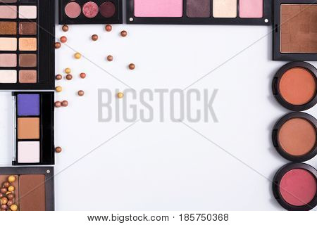 Makeup cosmetics and essentials frame on white background. Top view, flat lay with copy space. Beauty tools palettes collection, lipstick, eyeshadow, blush, foundation and more