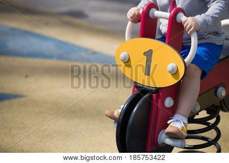 Toddler boy sitting on swing car and keeping balance. Child playing on outdoor playground on a sunny summer day.