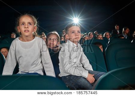 Low angle shot of little kids watching movie at the cinema looking amused and interested copyspace lens flare light childhood leisure activity people holidays carefree fascination concept.