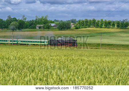 STEAM LOCOMOTIVE - Old train on a railway track among green fields