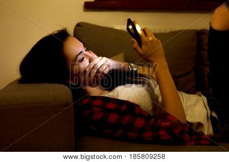 Young woman is lying on sofa and surfing in internet.