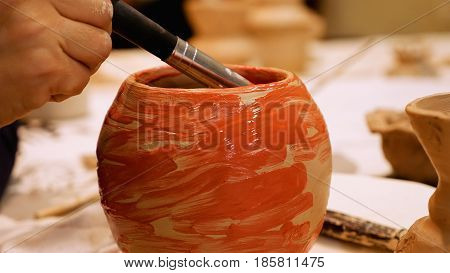 Art ceramist sculptor is painting clay pot or ceramics vase bowl to finish it. Art and handicraft modeling creation.