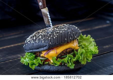 Black Burger with meat and cheese on a black wooden background