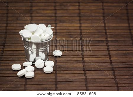 A large number of pills and medicine in a bucket on a dark wooden background