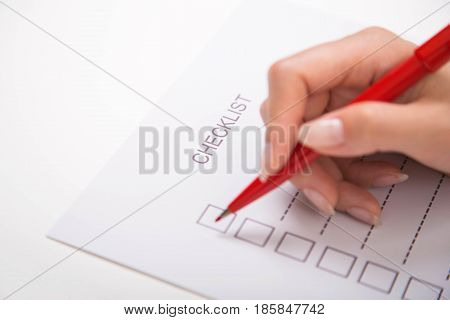 Close-up of hand marking on checklist with red pen