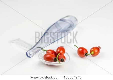 Rose hip on a medicine spoon on white background with the case of temperature indicator, symbolising that drinking and eating of rose hip products prevents diseases like flu, sore throat, high temperature etc.