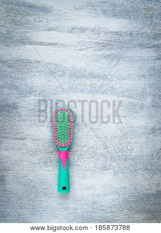 Green and pink hairbrush on a light wooden background
