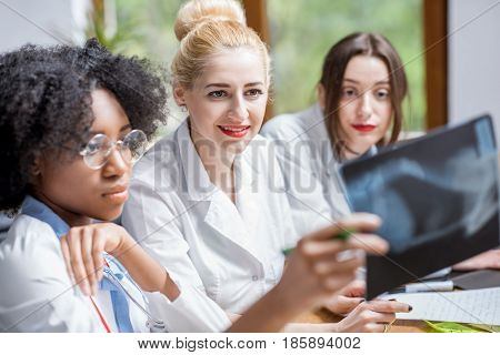 Multi ethnic group of medical students in uniform looking on the x-ray sitting at the desk in the modern classroom