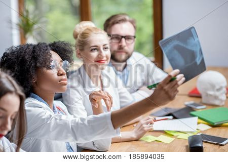 Multi ethnic group of medical students in uniform looking on the x-ray sitting at the desk in the modern classroom