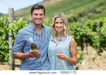 Portrait of young couple holding wine bottle and glass at vineyard
