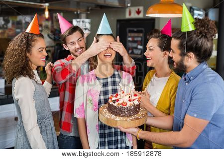 Happy friends with cake giving suprise to woman during her birthday