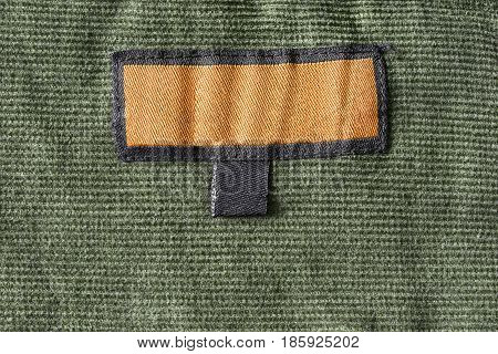 Blank yellow clothes label on khaki velvet background closeup