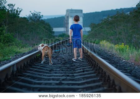 Handsome cute boy in blue shirt together with slobbery english bull dog standing on rail ways.Two friends boy and dog together