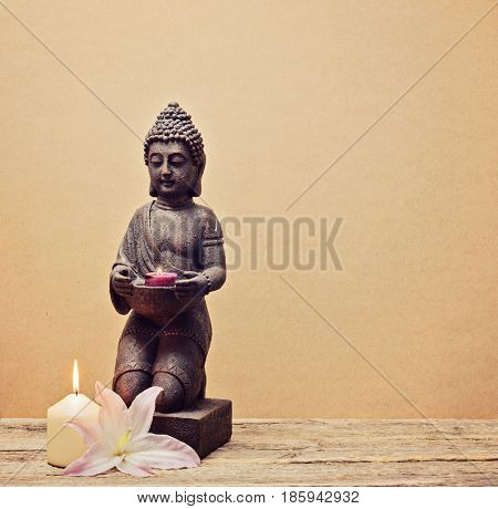 Buddha statue with candle in hands on a wooden background toned square