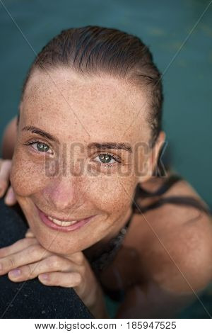 Vertical close-up portrait of beautiful girl with sunspots and wet hair in water