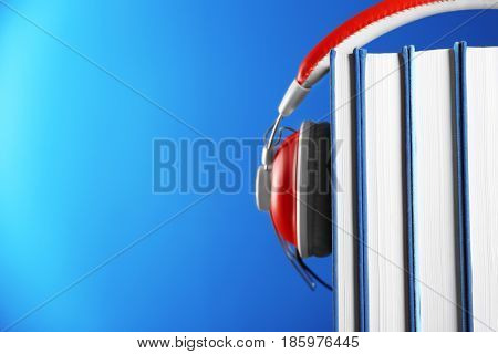 Audiobook concept. Pile of books with headphones on color background