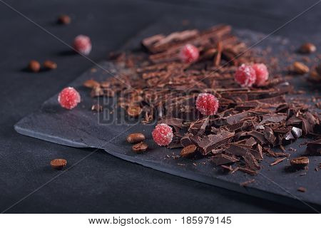 Dark chopping chocolate black roasted coffee beans red berries with spices on slate board over black textural background. Chocolate dessert confectionery and sweets concept