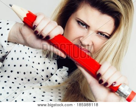 Angry mad woman blonde student girl or female teacher Stressed business worker releasing tension by breaking big red pencil. Studio shot on grey