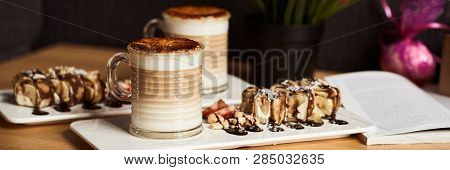 Banner Size Image Of Two Cups Of Hot Latte With Baked Caramel Crust And Sweet Roll With Banana And S