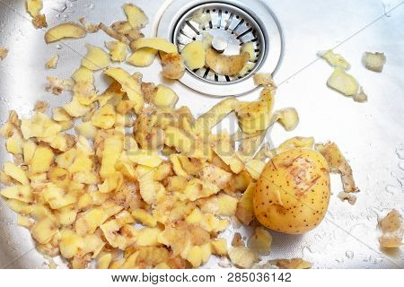 A Tuber Of Potato And A Lot Of Potato Peells In The Kitchen Sink - Cooking Food And Homework Concept