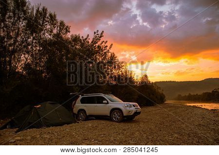 Camping At Rivershore On Sunrise. White Suv Car. Lifestyle