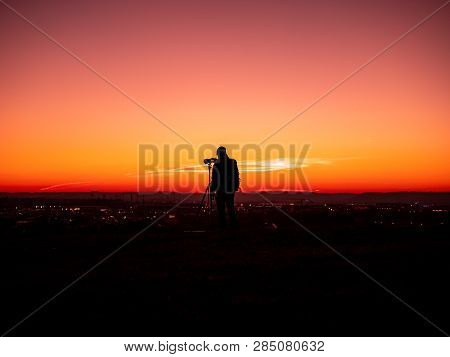 Image Of A Silhouette Of A Man With Tripot And Camera Standing On A Hill During Colorful Sunset