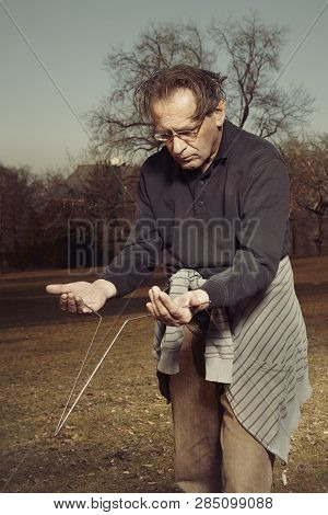 Man In Ugly Style Dress Practicing In Dowsing With Rods