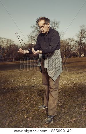 Man In Ugly Style Dress Practicing In Dowsing With Rods