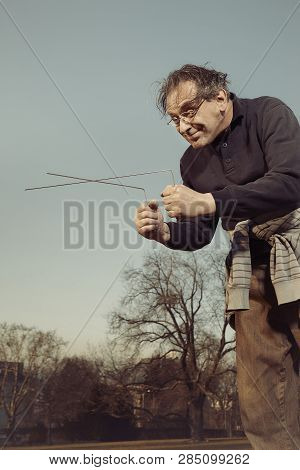 Man In Ugly Style Dress Practicing In Dowsing With Rods