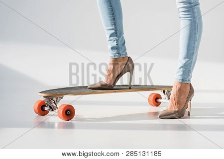 Cropped View Of Woman In Jeans And High-heeled Shoes Standing On Lonboard On Grey Background