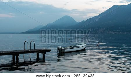 Beautiful Landscape On Lake Garda In Italy. Boat Near The Pier On The Water Surface Of The Water. Th