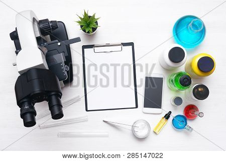Laboratory Table With A Blank Paper Sheet Of Researching Results, Microscope, Mobile Phone And A Che