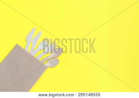 Disposable Tableware From Natural Materials, Wooden Spoons, Knives, And Forks In Paper Bag On Yellow