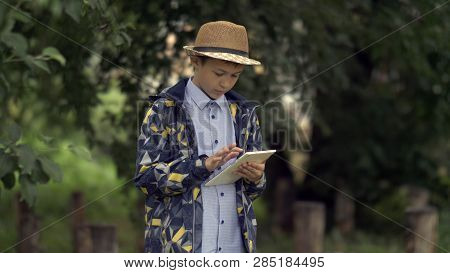 Farmer Boy In A Hat Uses A Tablet In The Garden
