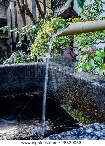 A Bamboo Pipe Pours Overflow Water Out Of A Japanese Hot Spring Bath On The Side Of Oyama, A Mountai