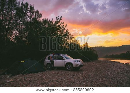 Camping At Rivershore On Sunrise. White Suv Car. Lifestyle