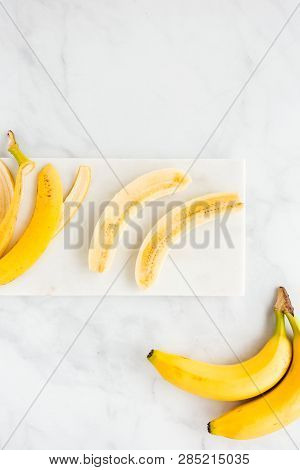 Banana Peel And A Peeled Banana Cut Lengthwise In Half On White Marble Board And Background. Top Vie