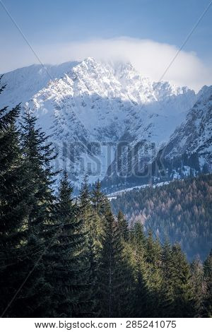 Some Clouds Around Snow Covered Mountain Peak Grimming And Forest Near Tauplitz On A Sunny Winter Da