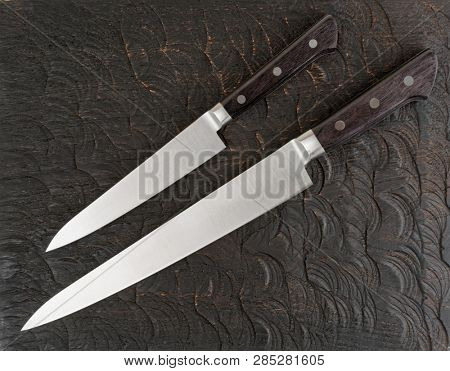 Two nww kitchen knives on black wooden board shot from above