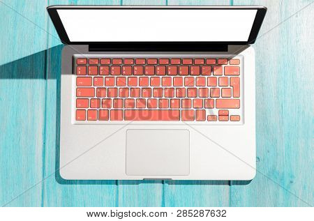 Laptop with living coral colored keyboard on wooden table on a sunny day, view from above