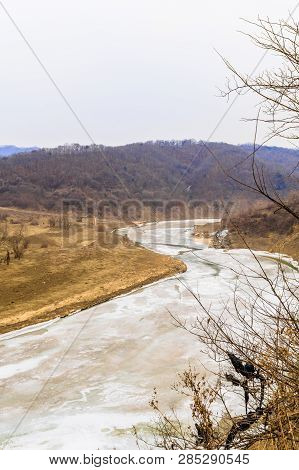 Winter Landscape Of Frozen River In Mountain Valley Under Gray Sky.