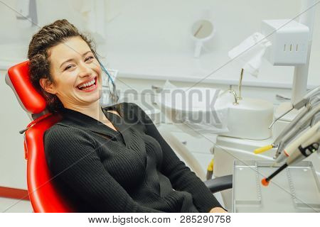 Woman At The Reception Of A Dentist In A Dental Clinic. She Sits In A Red Chair. Happy Patient And D