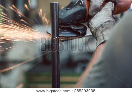 Worker in metal factory grinding workpiece with disk grinder, sparks flying