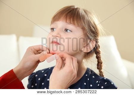 Nurse Applying Medical Patch To Little Girl's Injured Face Indoors. First Aid
