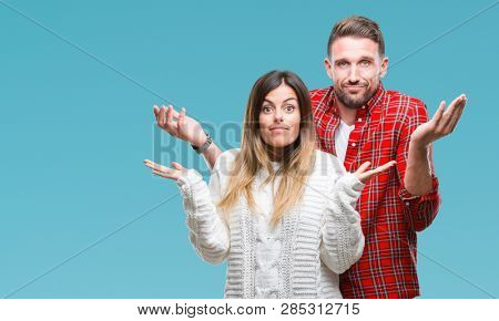 Young couple in love wearing winter sweater over isolated background clueless and confused expression with arms and hands raised. Doubt concept.