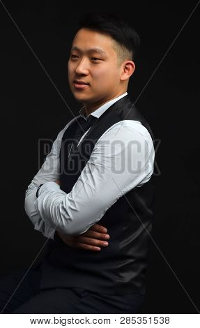 Photo Of An Asian Man Standing On A Black Background, Dressed In A Shirt And A Vest, Looking Sideway