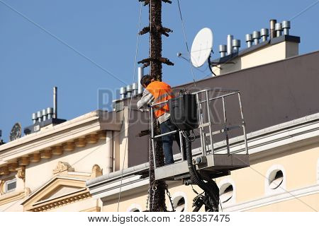 The Worker In Overalls Works At Height In A Building Mechanical Lifting Basket. Repair And Construct