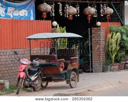 Cambodia, Siem Reap 12/08/2018 A Little Asian Girl Sits In A Moto Rickshaw Near A House With Red Lan